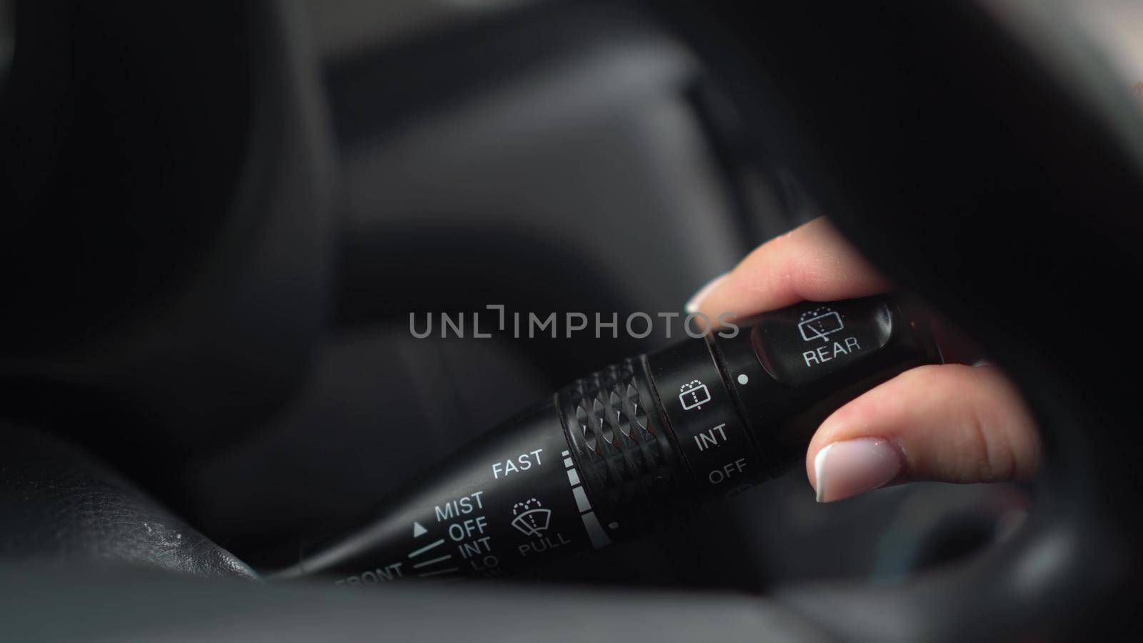 A woman turns on the wipers by turning the lever in the car. Automotive panel close-up. 4k