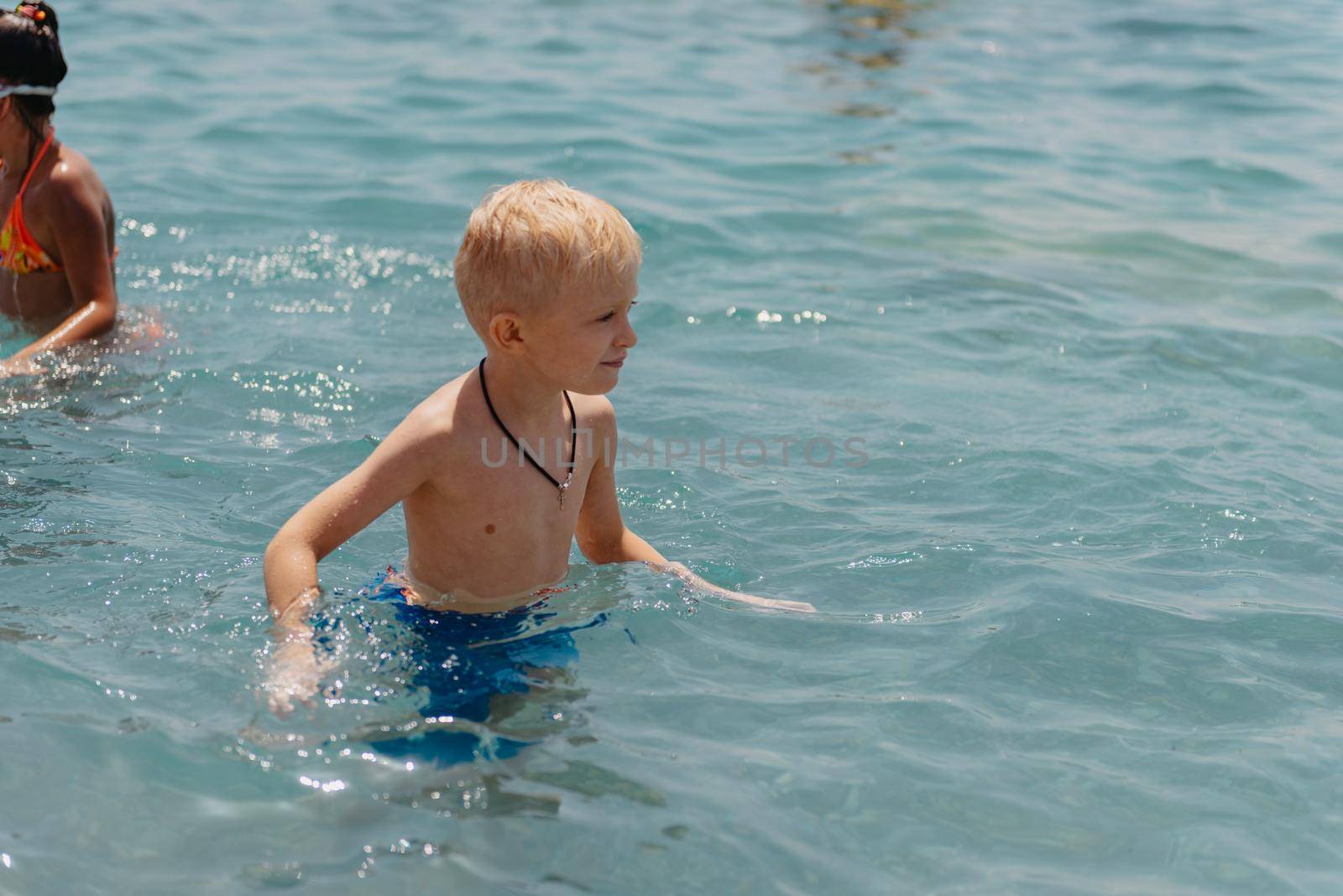 Child learning to swim in the open sea of tropical resort. Kids learn swimming. Exercise and training for young children. Little boy with colorful float board in sport club. Swimming baby or toddler. Happy child boy swims in sea in swimming circle with splash. Blue sky and water. Swimming training. Fun joy activities on vacation in the beach. Childhood moments lifestyle. Freedom careless. boy swim in the sea by Andrii_Ko