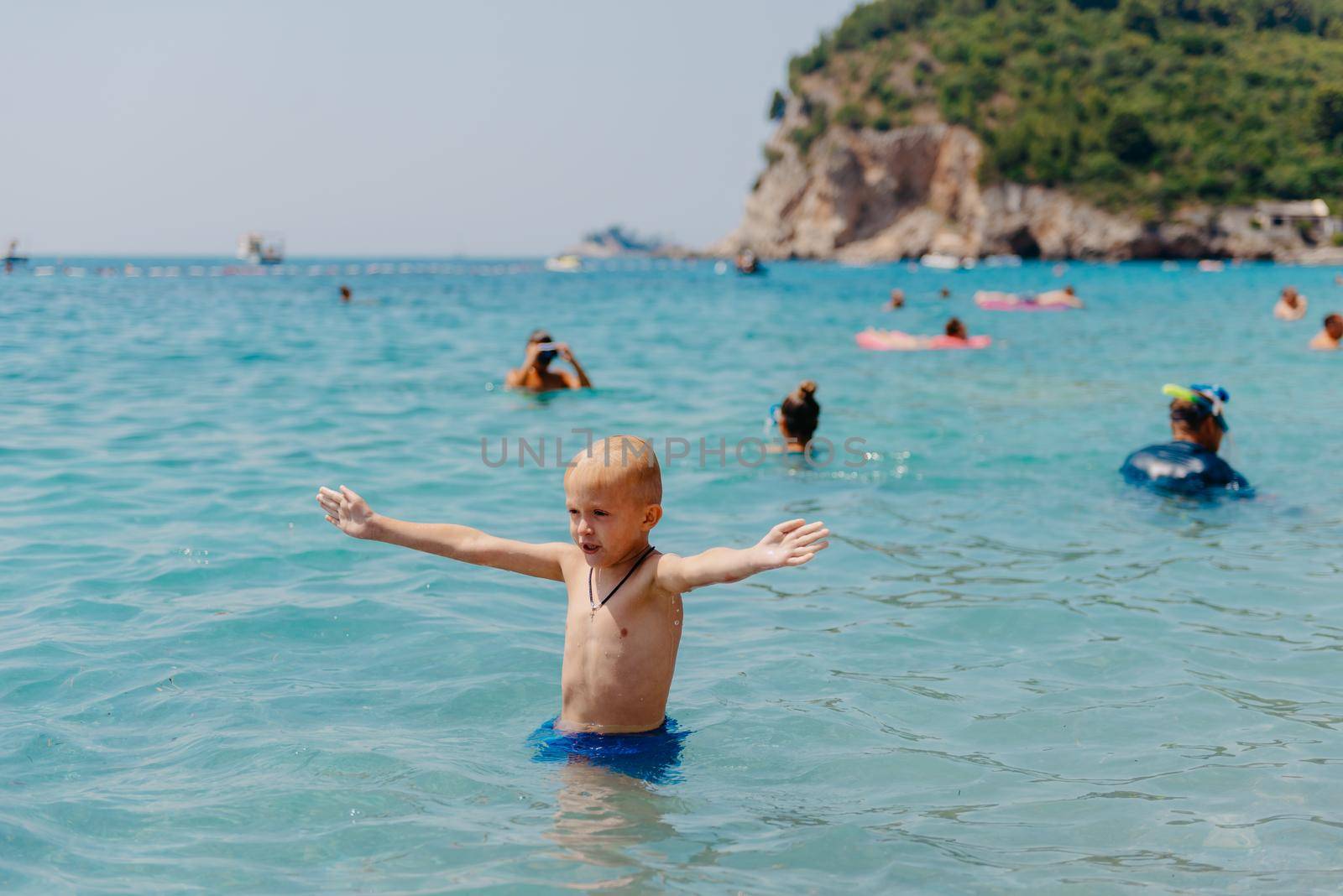 Child learning to swim in the open sea of tropical resort. Kids learn swimming. Exercise and training for young children. Little boy with colorful float board in sport club. Swimming baby or toddler. Happy child boy swims in sea in swimming circle with splash. Blue sky and water. Swimming training. Fun joy activities on vacation in the beach. Childhood moments lifestyle. Freedom careless. boy swim in the sea.