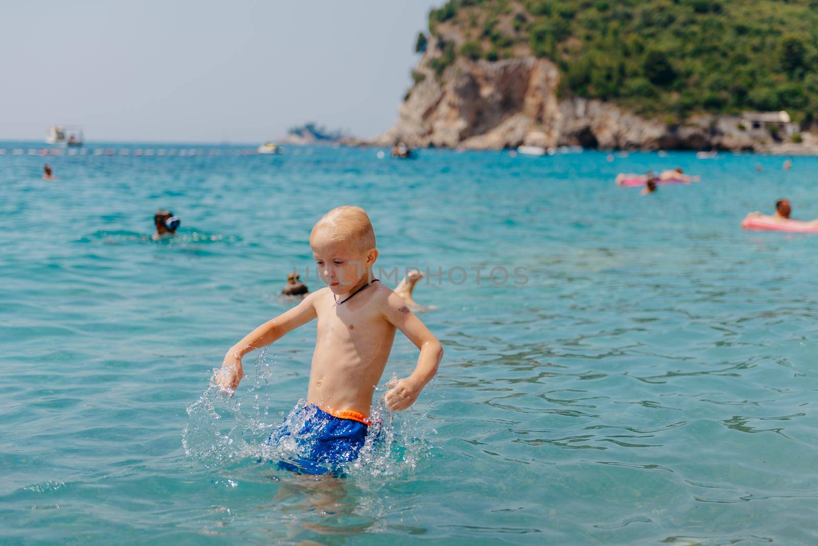 Child learning to swim in the open sea of tropical resort. Kids learn swimming. Exercise and training for young children. Little boy with colorful float board in sport club. Swimming baby or toddler. Happy child boy swims in sea in swimming circle with splash. Blue sky and water. Swimming training. Fun joy activities on vacation in the beach. Childhood moments lifestyle. Freedom careless. boy swim in the sea by Andrii_Ko