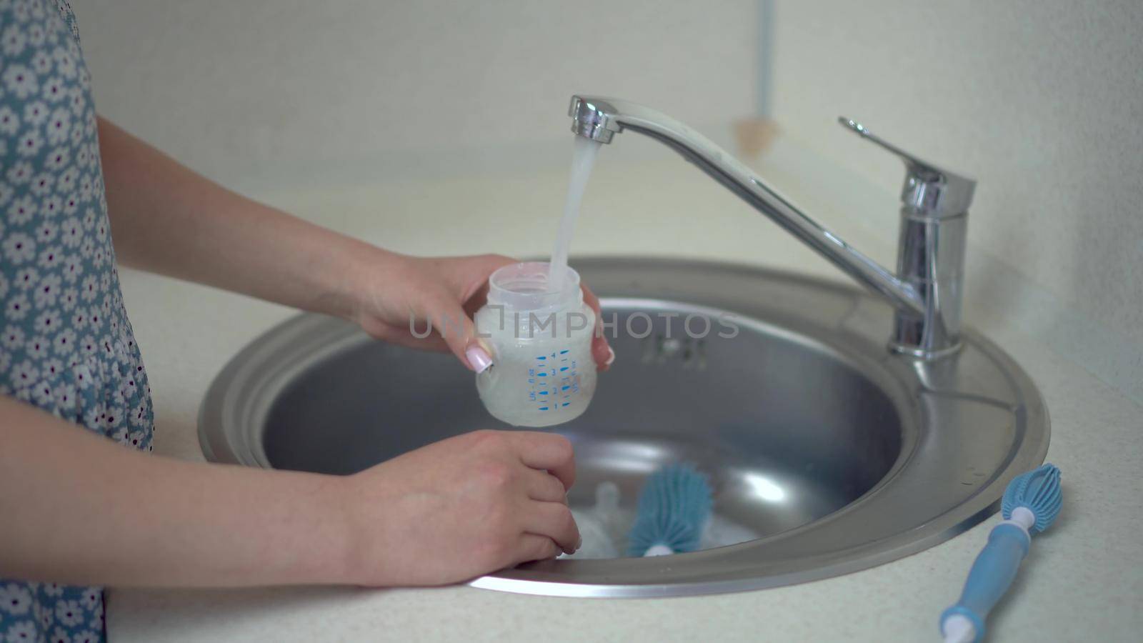 A young mother washes a bottle of baby food with a special brush. Close-up hands. 4k