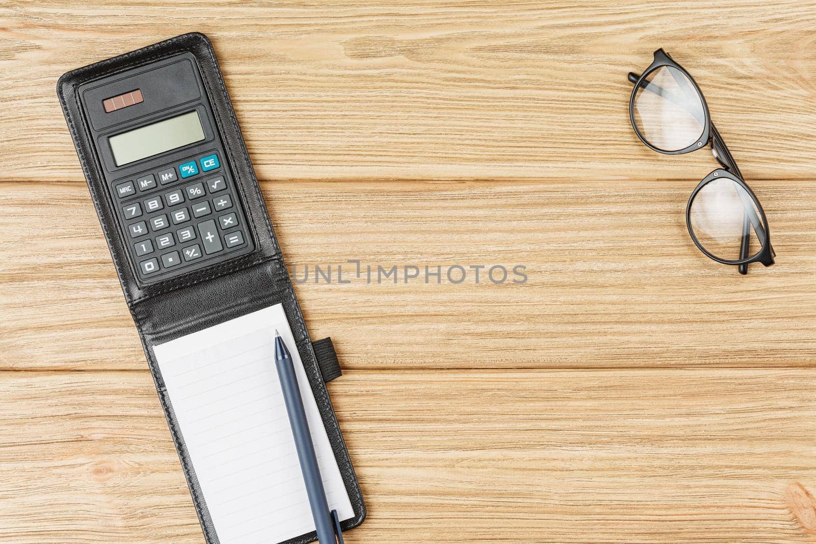 Black leather case with calculator and notebook dark blue pen and glasses on a light wooden background top view.