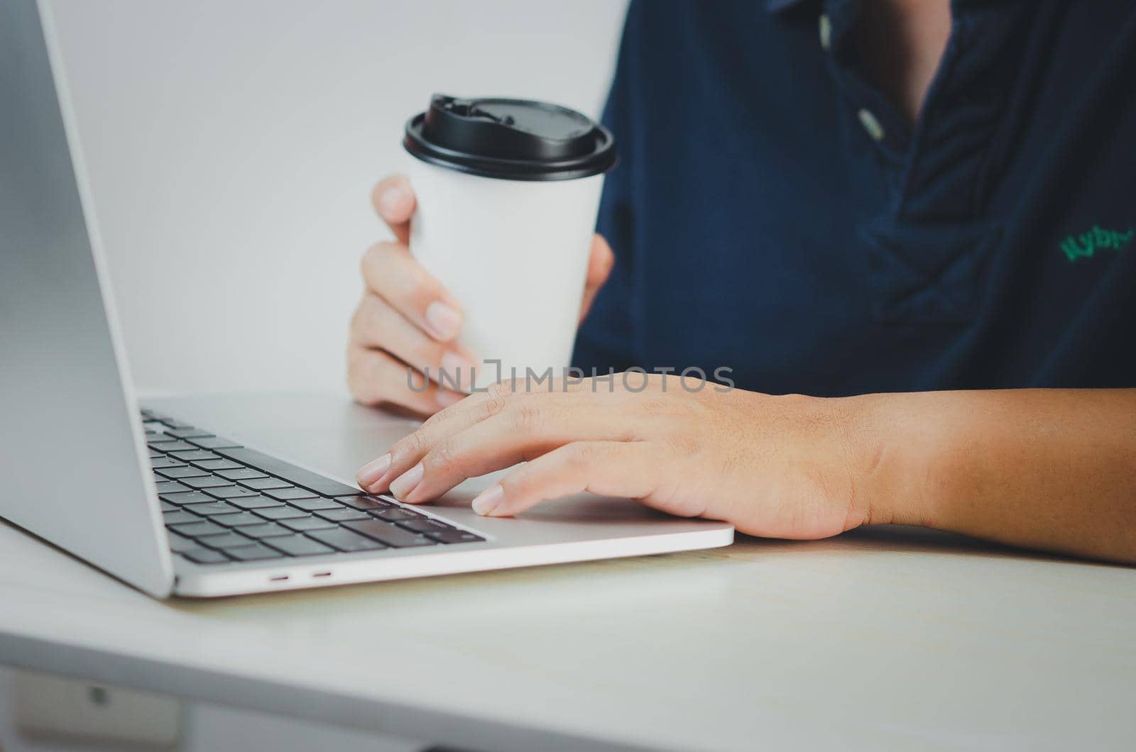 man using computer laptop and coffee cup paper searching internet, sending sms, using text messenger or online banking on desk.