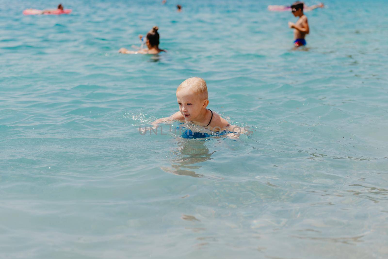 Child learning to swim in the open sea of tropical resort. Kids learn swimming. Exercise and training for young children. Little boy with colorful float board in sport club. Swimming baby or toddler. Happy child boy swims in sea in swimming circle with splash. Blue sky and water. Swimming training. Fun joy activities on vacation in the beach. Childhood moments lifestyle. Freedom careless. boy swim in the sea by Andrii_Ko