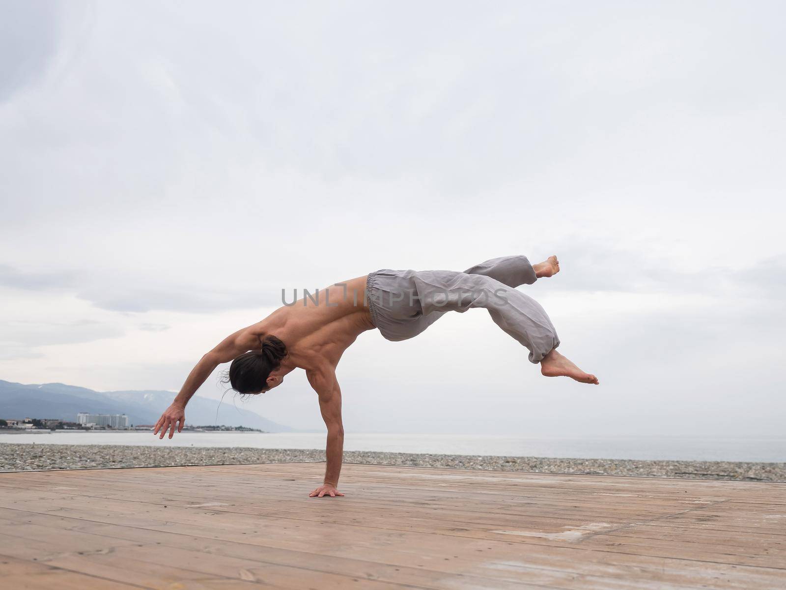 Shirtless caucasian man doing backflip on pebble beach