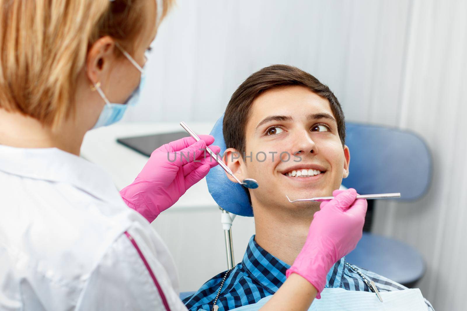 Handsome young man is having dental check up in dental office. Dentist is examining a patient teeth with dental tools. Dentistry