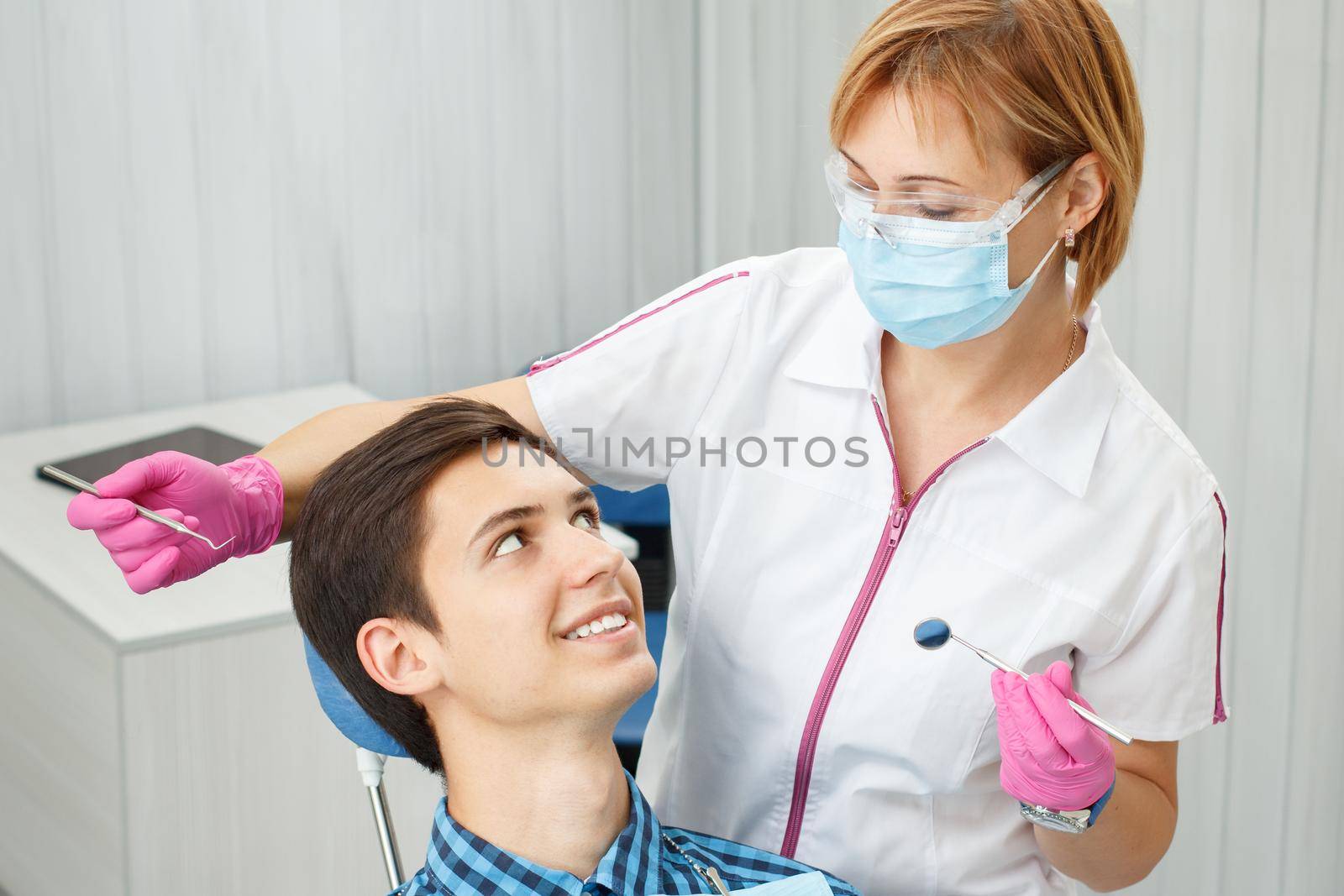 Female dentist and young man in dentist office. Handsome young man is having dental check up in dental office