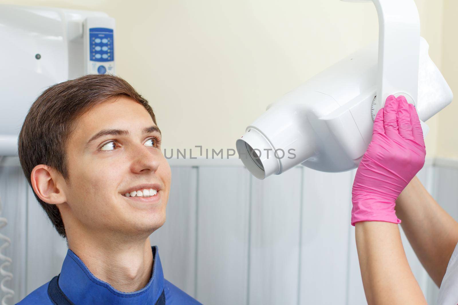 Female dentist is going to make teeth x-ray image for handsome young man in dental clinic. Using dental x-ray machine in dental office. Dental equipment