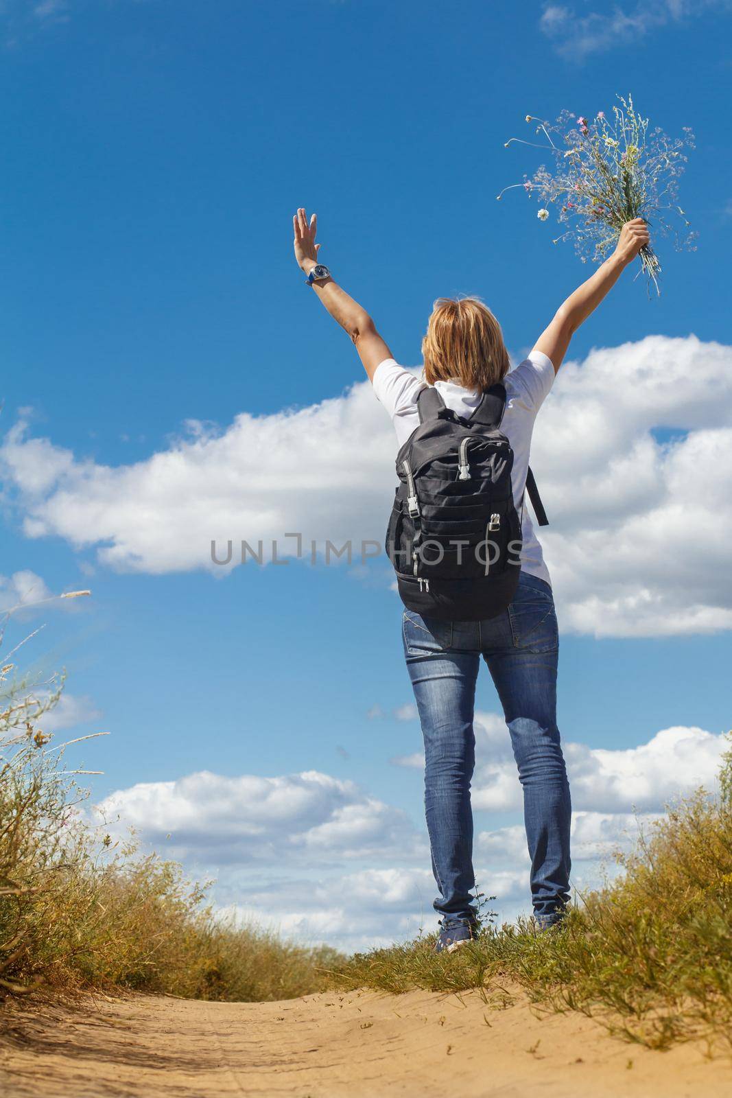 Young lady walking on a rural road. Hiker with backpack walking outdoors in nature. Traveler walking along country trail outdoor. Healthy active lifestyle