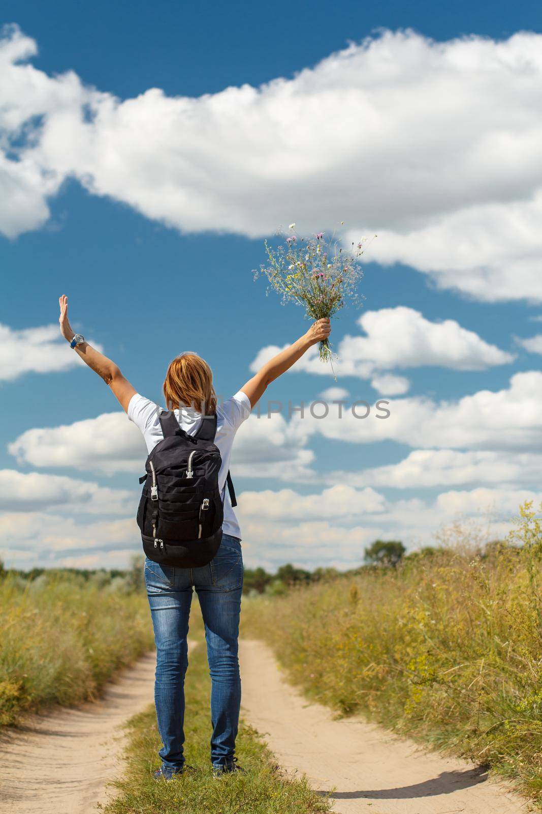 Young lady walking on a rural road. Hiker with backpack walking outdoors in nature. Traveler walking along country trail outdoor. Healthy active lifestyle