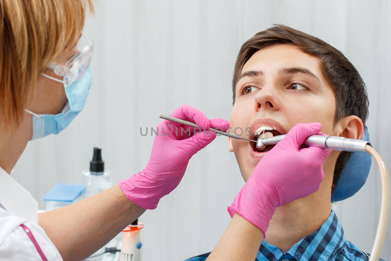 Female dentist is treating a patient tooth in dental office with focus on patient mouth. Dentistry