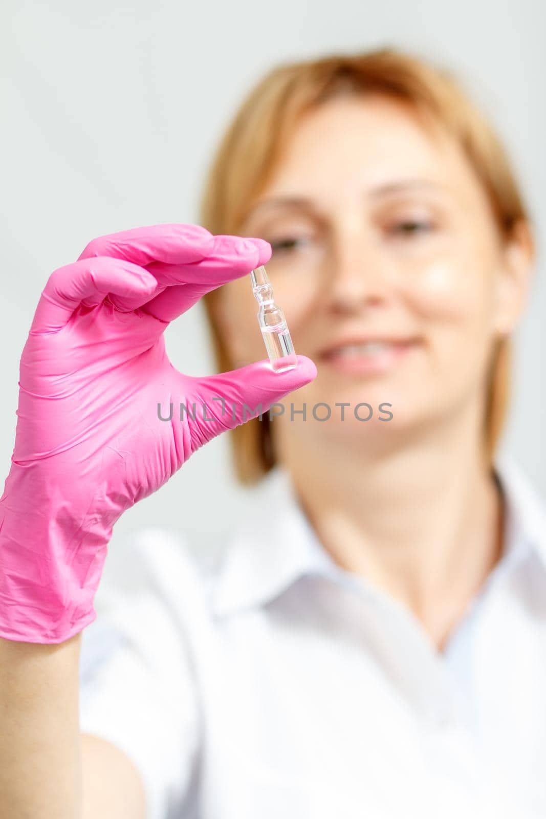 Smiling female doctor in pink glove holding ampoule with medicine. Selective focus on ampoule