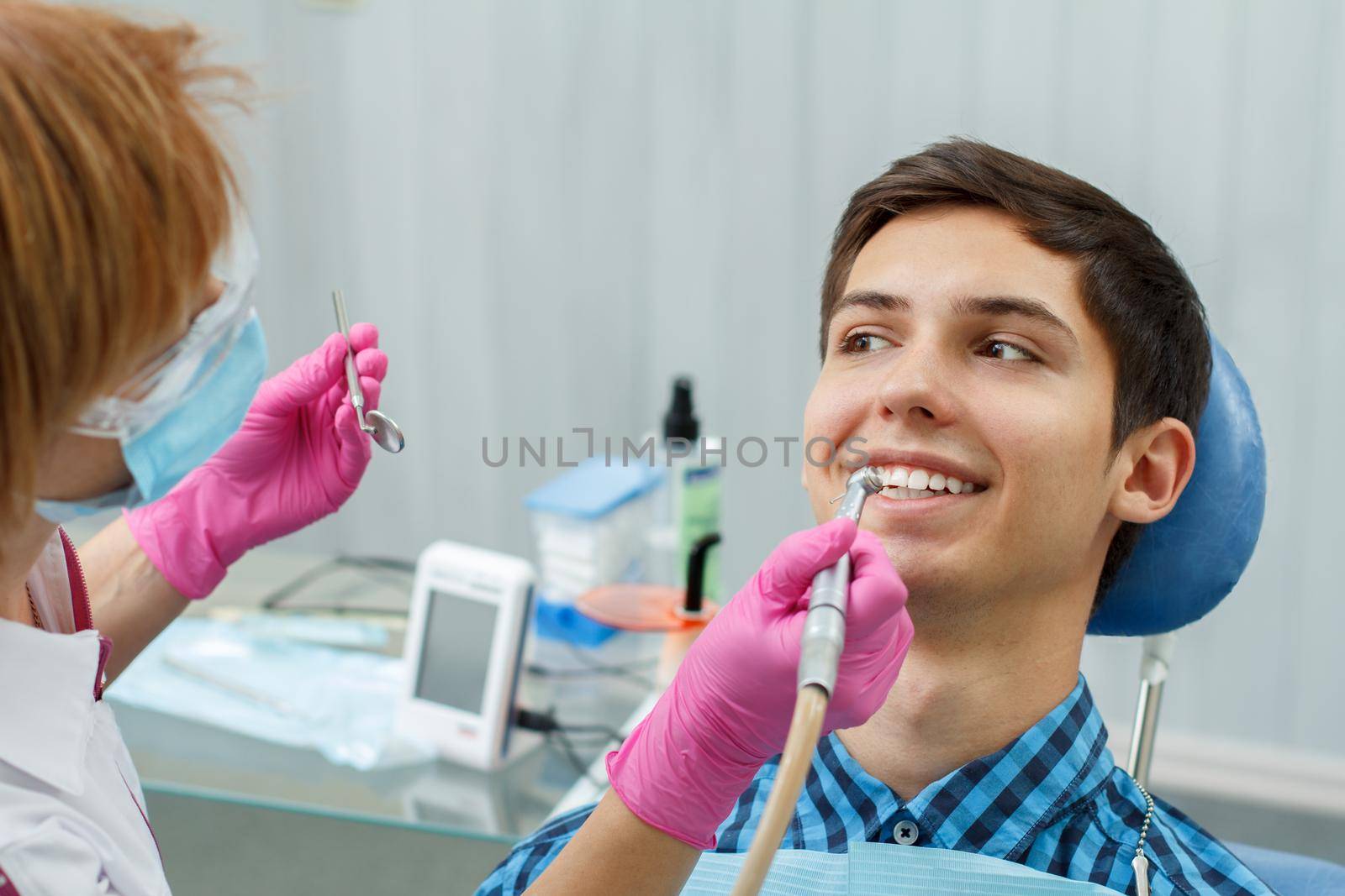 Female dentist treating a patient tooth in dental office with focus on patient mouth by mvg6894