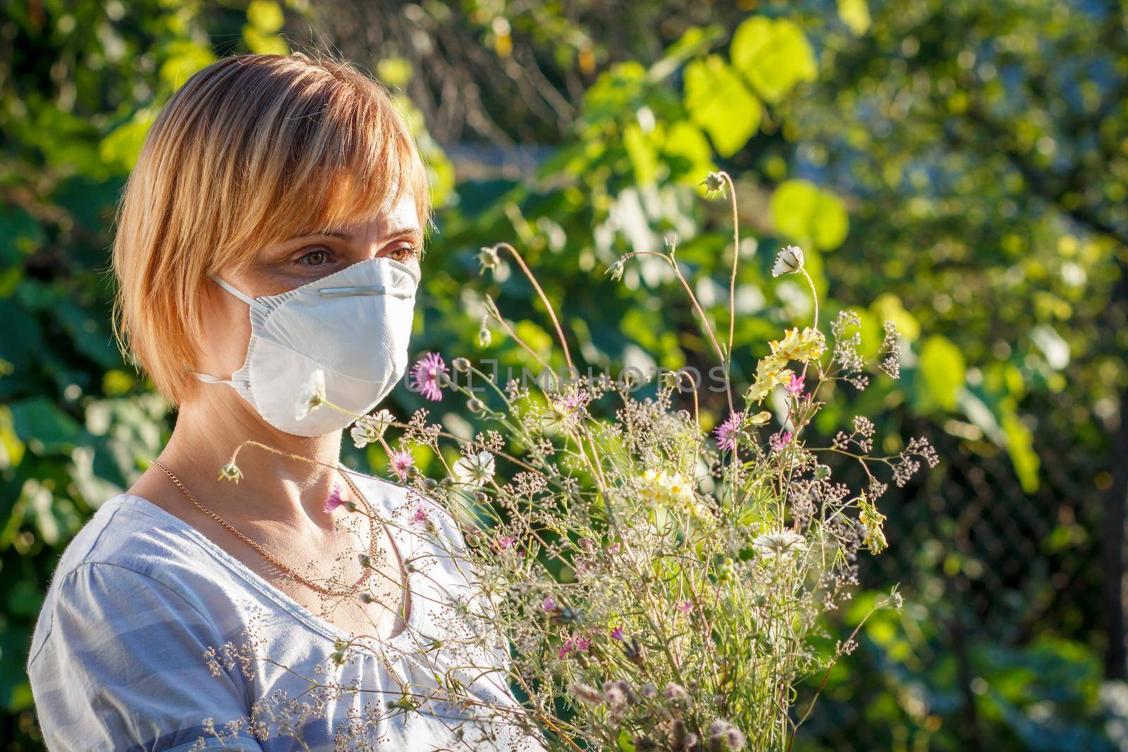 Woman in protection mask holding bouquet of wildflowers and trying to fight allergies by mvg6894