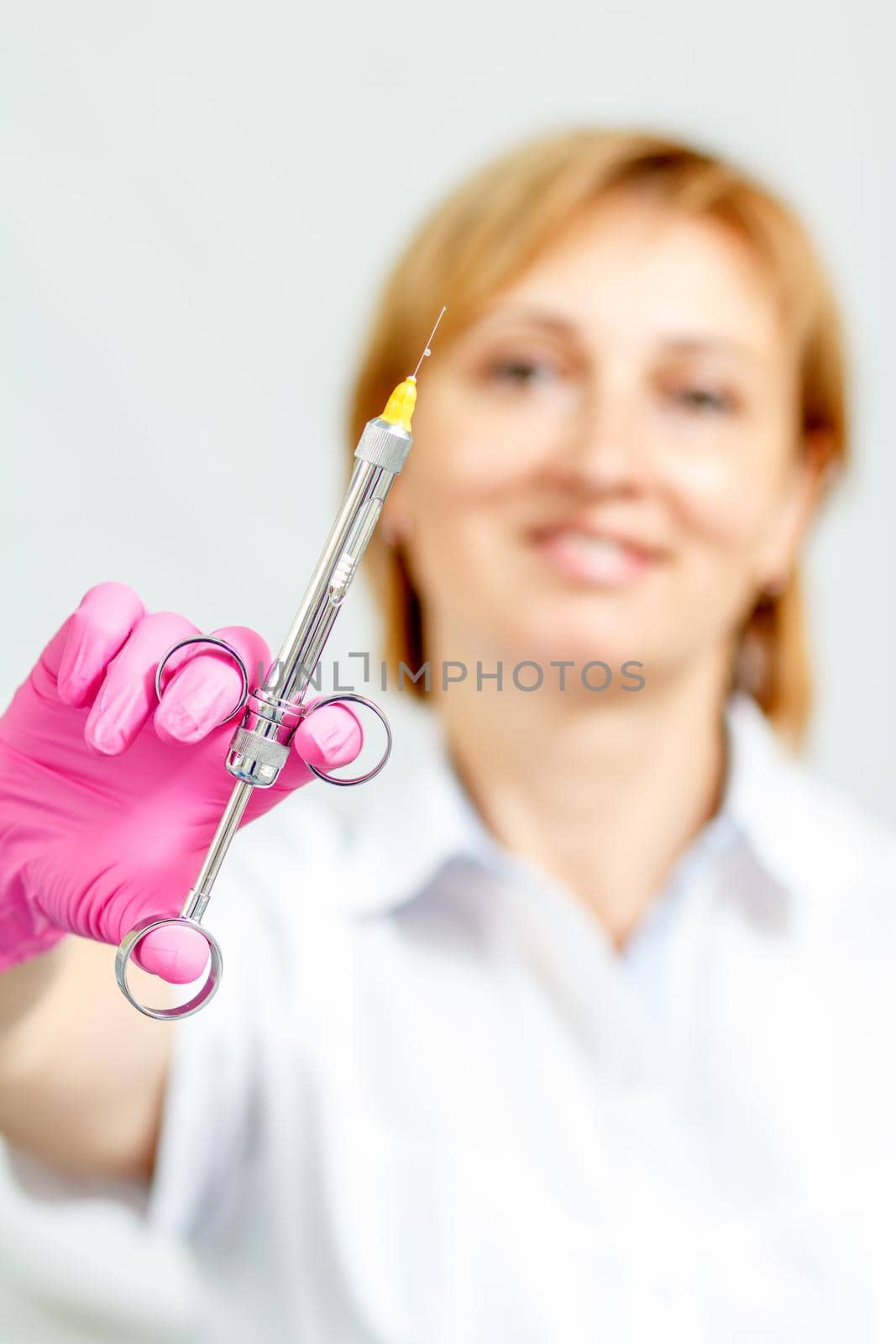 Smiling female doctor in pink glove holding syringe with anesthetic and needle. Selective focus on syringe