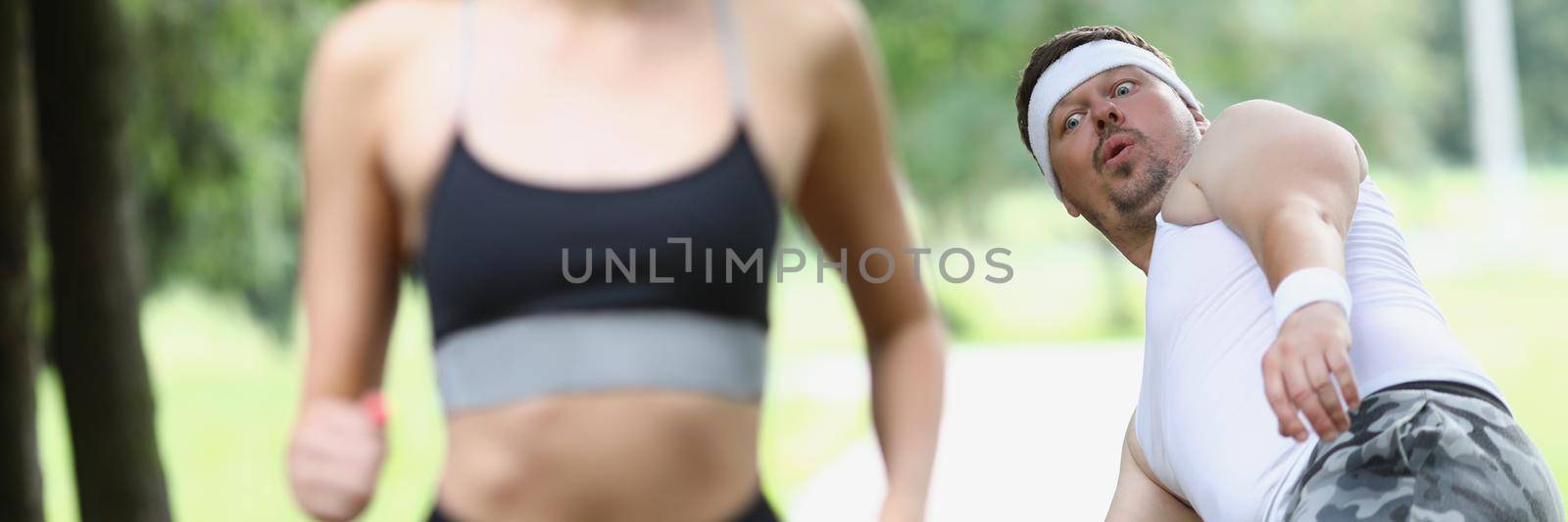 Portrait of tired sweaty middle aged man fall from beauty of young woman. Active woman jogging in front, feeling energetic. Sport, healthy habit concept