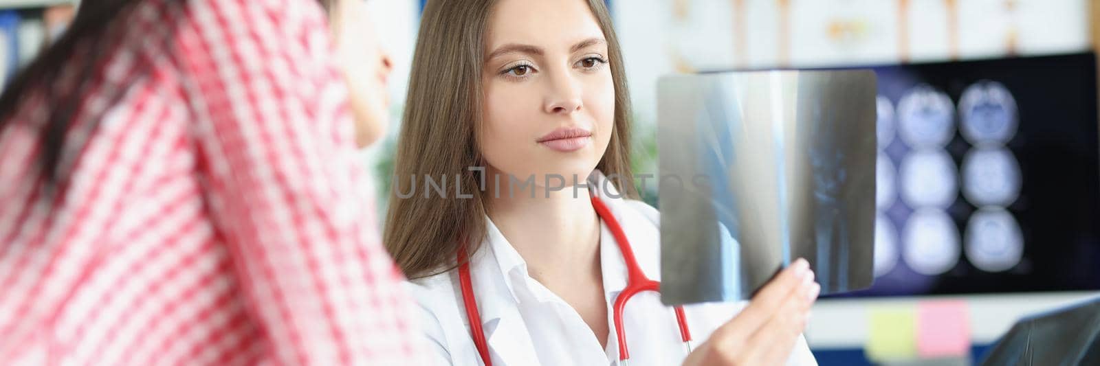 Portrait of clever professional doctor examine x ray result on appointment, show patient. Medical worker describe scan to client. Health, checkup concept