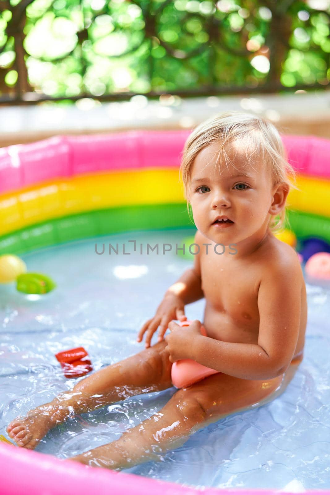 Little girl sits in an inflatable pool on the balcony with a toy. High quality photo