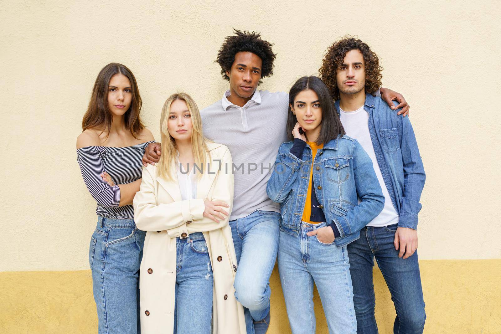 Multi-ethnic group of friends posing together outdoors against a yellow urban wall.