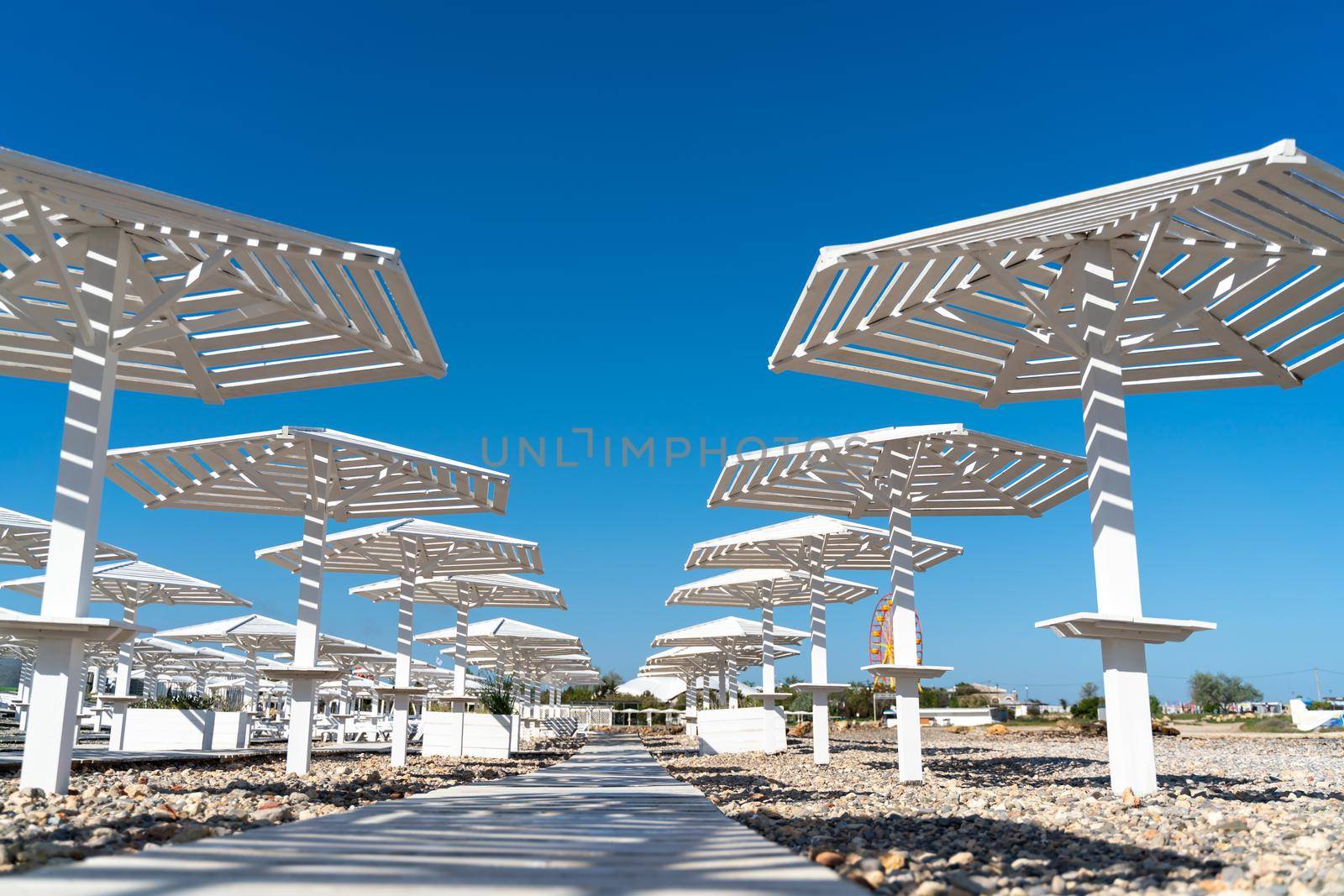 Rows of wooden umbrellas from the sun on the seashore in the morning. Wooden paths on the sand between umbrellas. Beach holiday at the resort