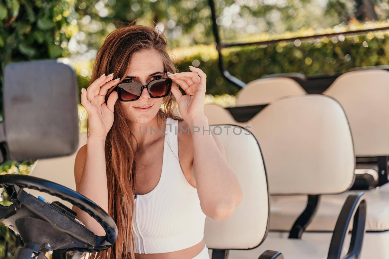 A middle-aged woman is driving a car for transporting tourists. Electric car, Tourist bus. Car for transporting people around the hotel, park, golf club by Matiunina