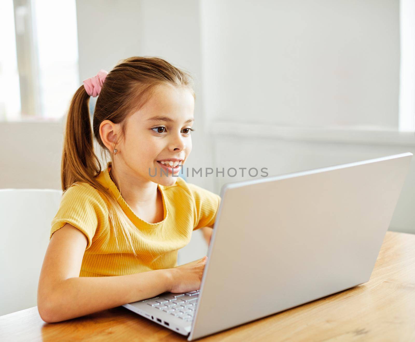 Portrait of a little girl having fun using laptop or doing homework with laptop at home