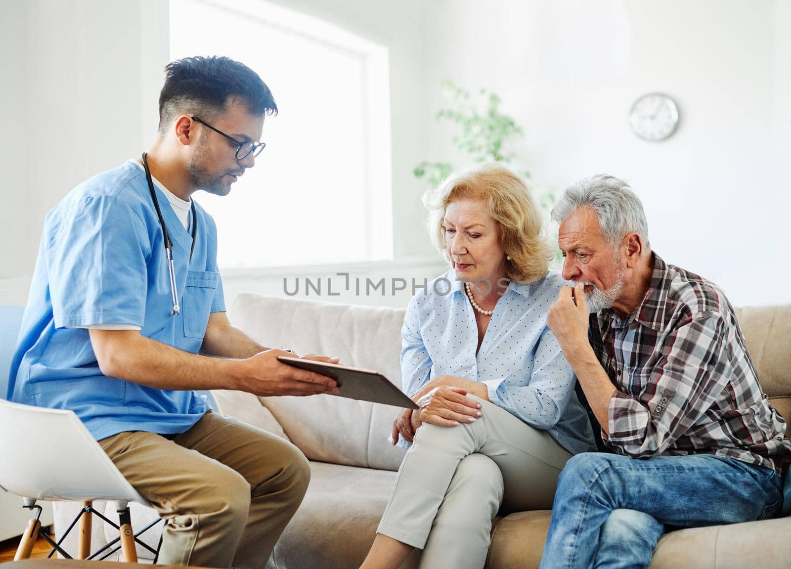 Doctor or nurse caregiver with senior couple using tablet at home or nursing home