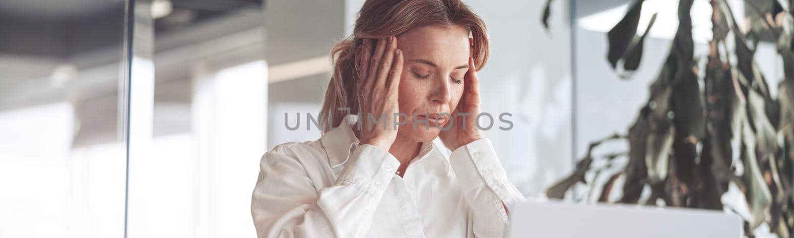 Confident businesswoman working on laptop at her workplace at modern office.Headache concept.