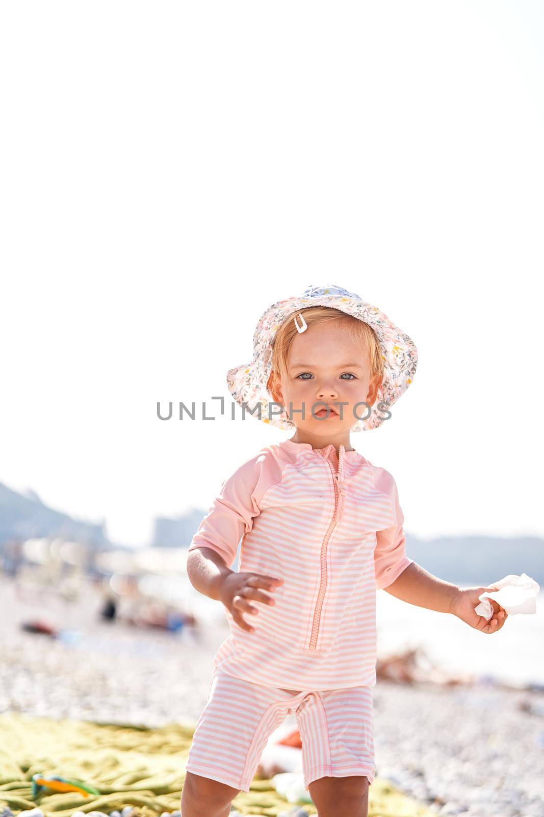 Little girl in a panama hat stands on a beach by Nadtochiy