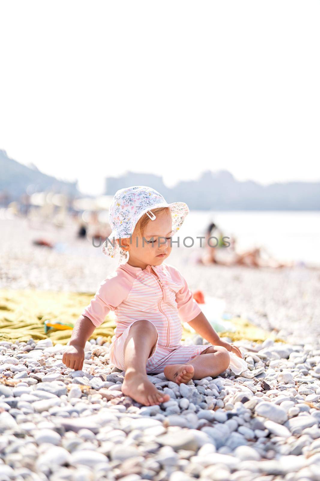 Little girl in a panama hat sits on a pebble beach. High quality photo