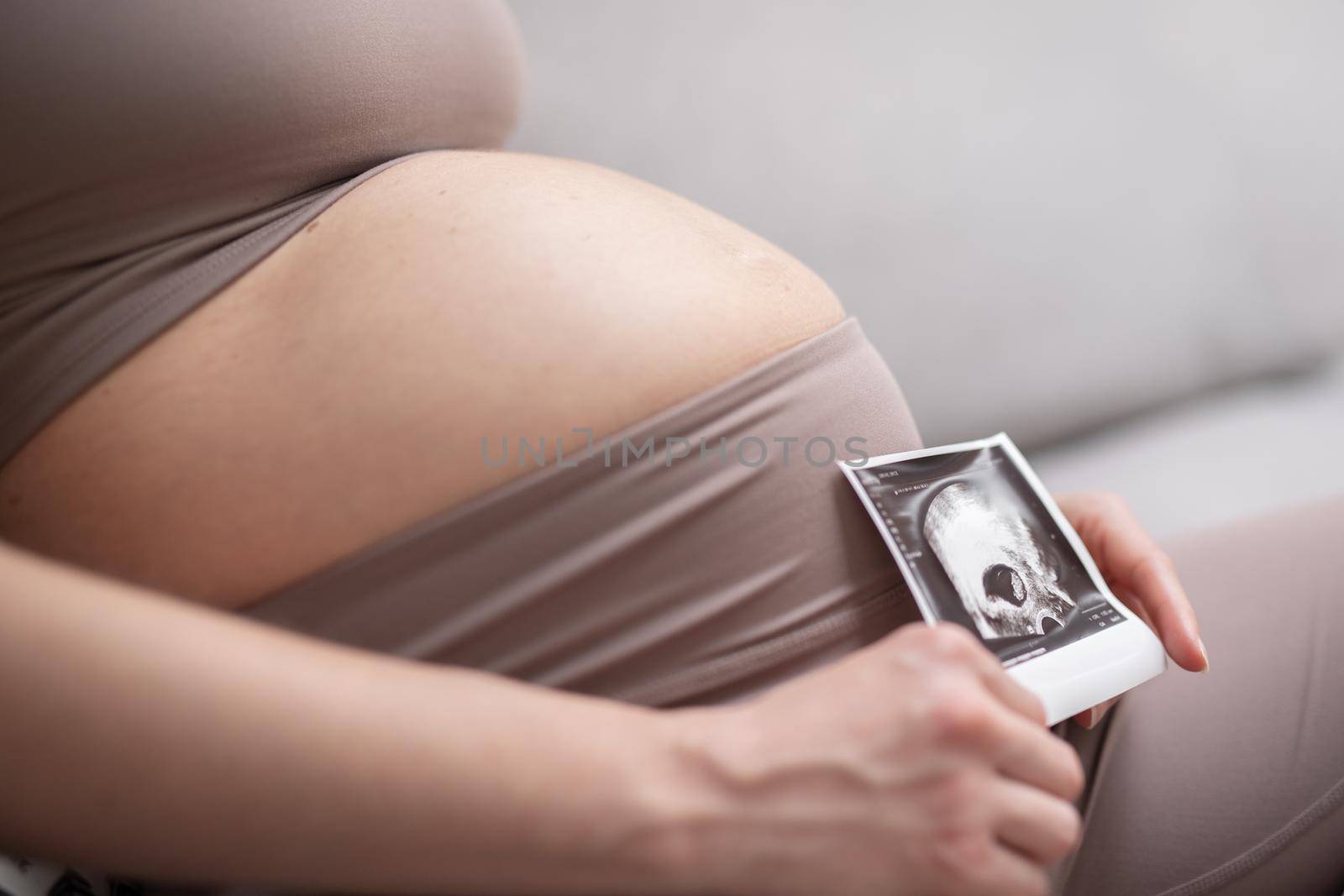 Pregnant woman belly. Pregnancy Concept. Pregnant tummy close up. Detail of pregnant woman holding ultrasound photo of her embrio baby.