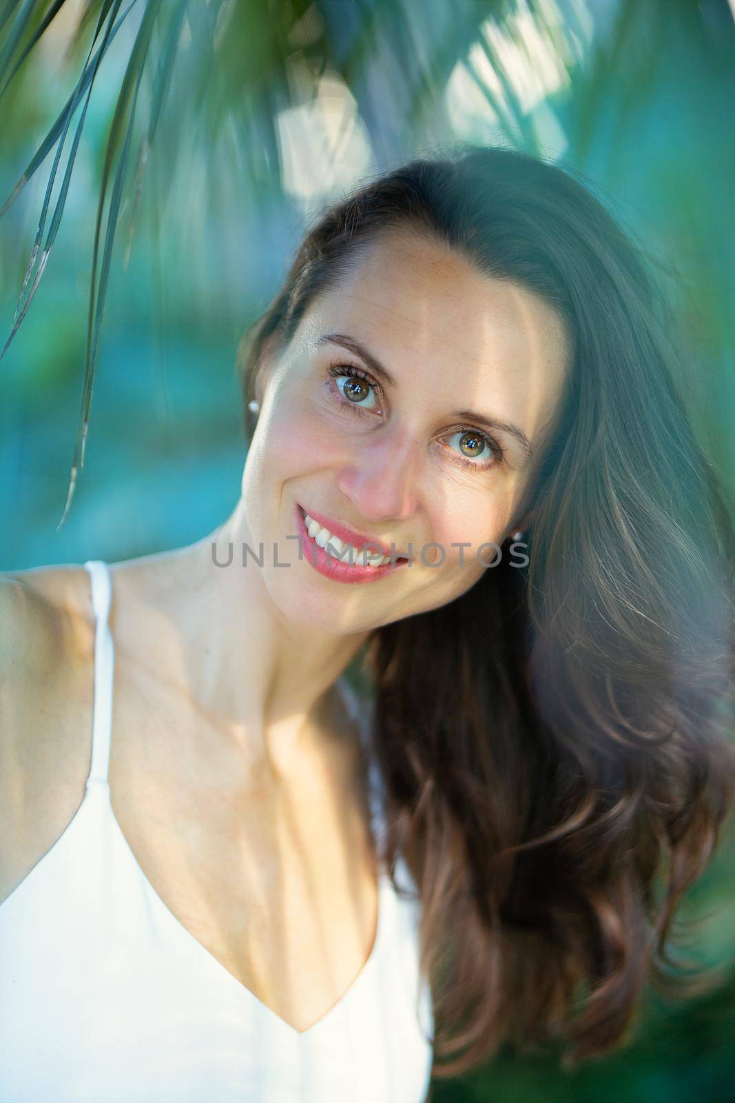 Young beautiful natural cheerful woman with healthy face and skin in exotic greenery. Closeup fresh face of attractive girl. Summer model. Natural beauty concept by kasto