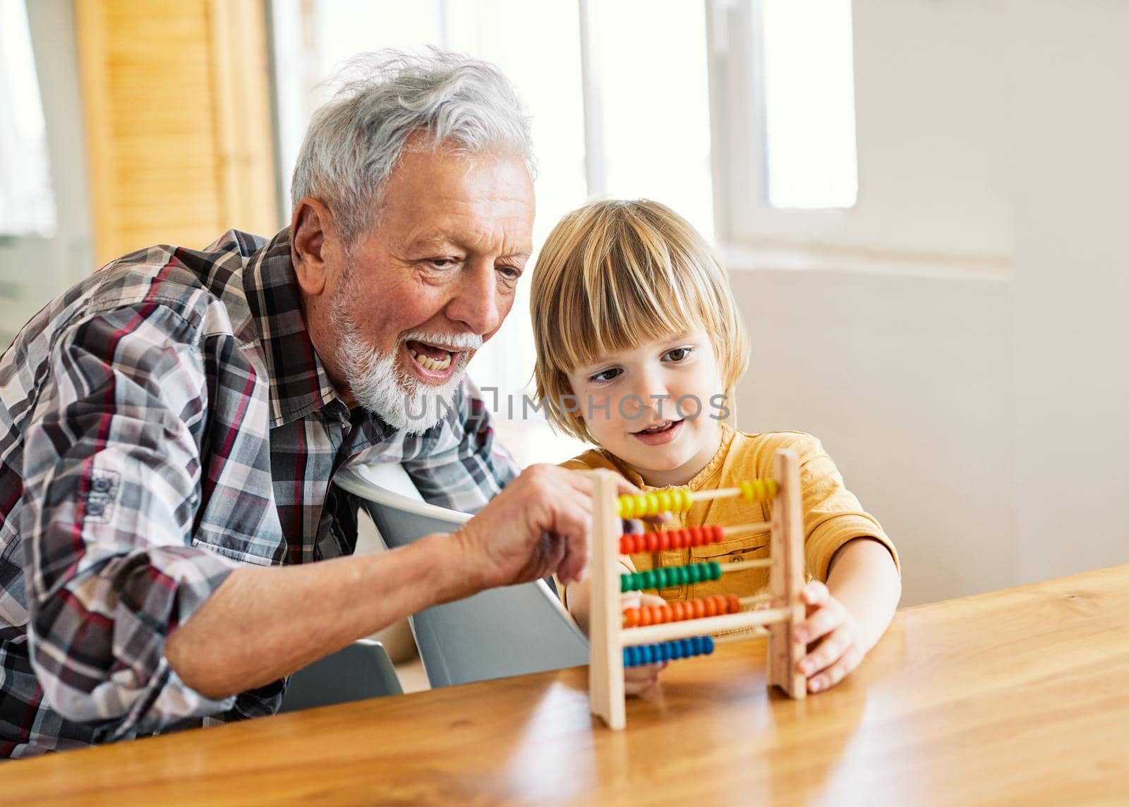 Portrait of grandfather and grandson having fun with an abacus tool or toy doing mathematic calculation and learning together at home