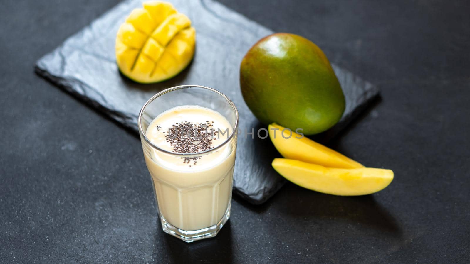 Cool mango milkshake on a black background. A drink to quench your thirst in the summer. Indian cuisine classic drink - Lassi. Milk, yogurt with mango chunks.