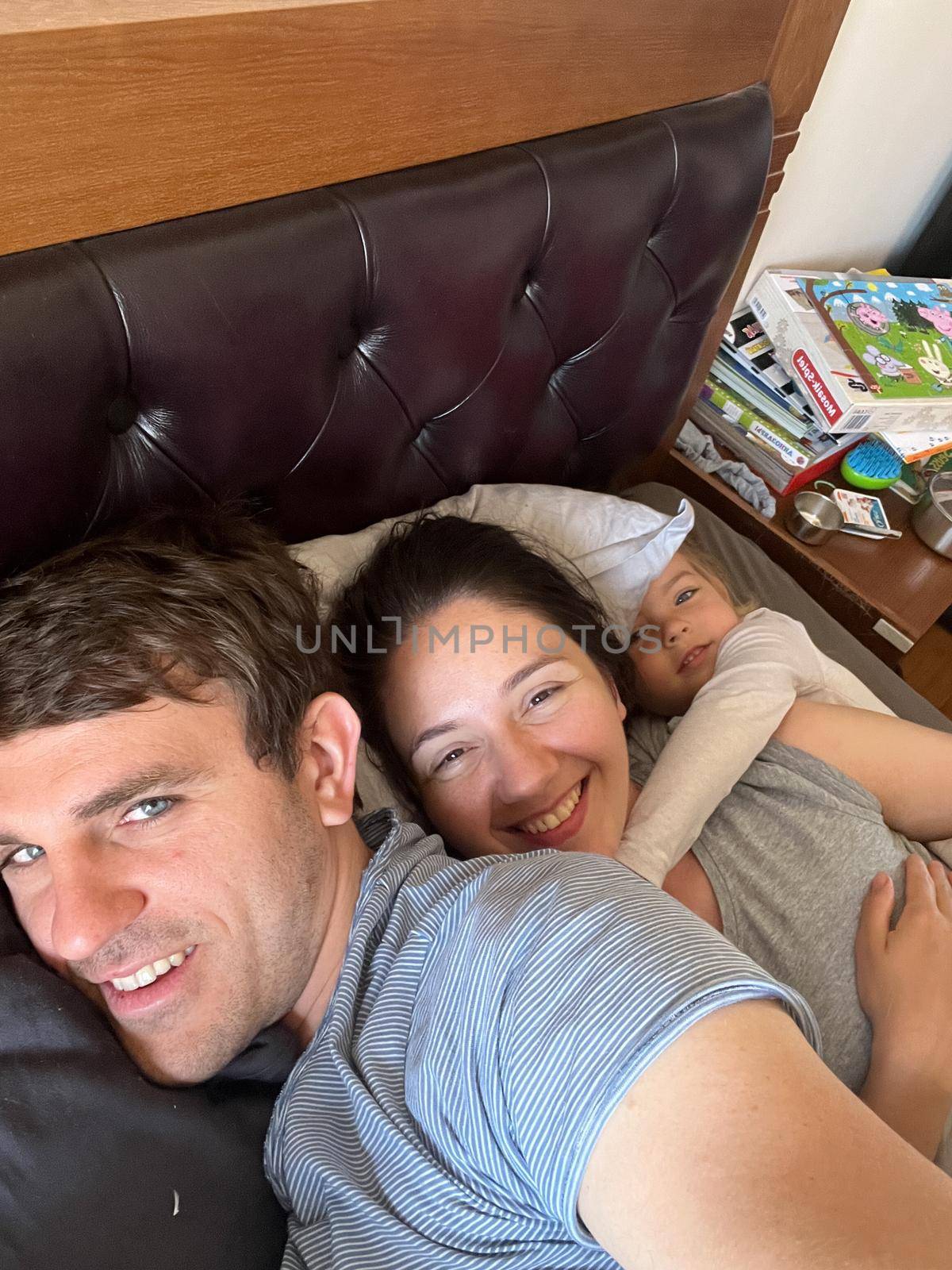 Mom, dad and little daughter lie in bed by Nadtochiy