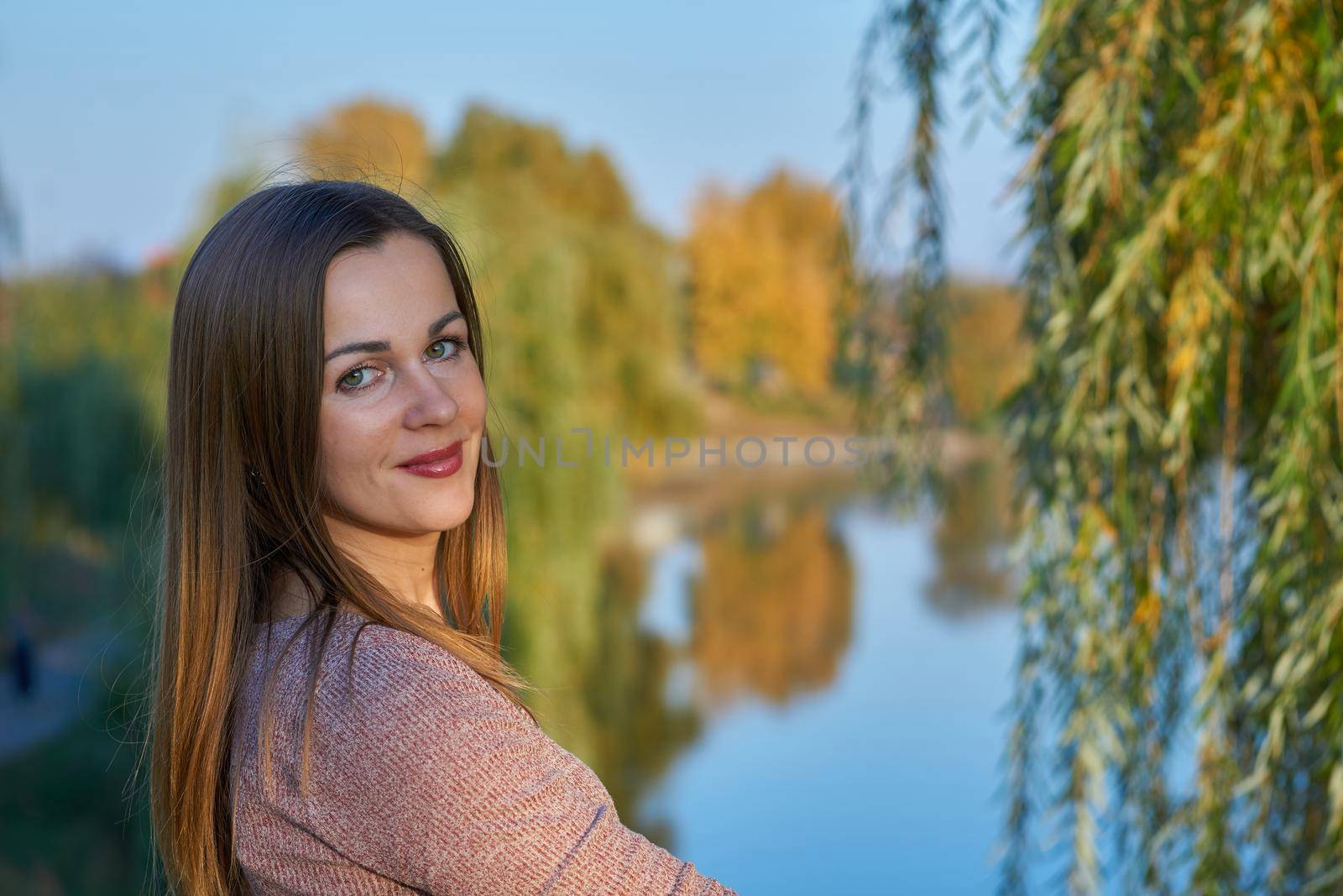 Young cheerful woman on the shore of a calm lake among golden autumn foliage by jovani68