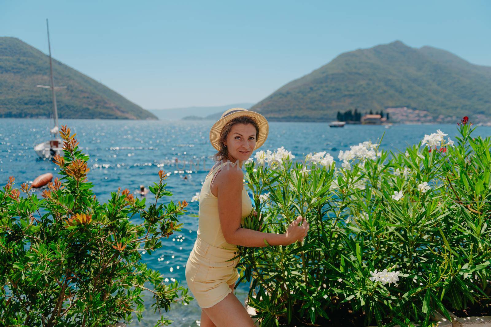 Summer photo shoot on the streets of Kotor, Montenegro. Beautiful girl in yellow dress and hat. smiling tourist girl with hat. Spectacular view of Montenegro with copy space. Ю fashion outdoor photo of beautiful sensual woman with blond hair in elegant dress and straw hat and bag, posing in Montenego's city Perast.