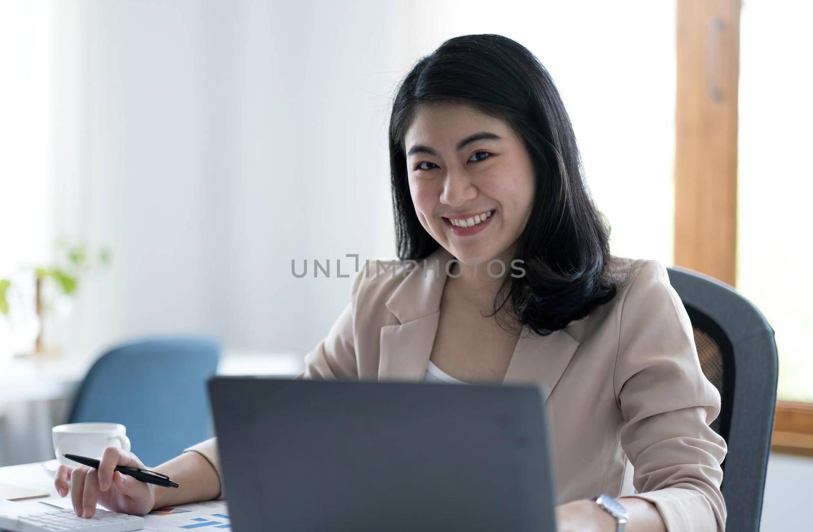 Charming Asian woman working at the office using a laptop Looking at the camera. by wichayada