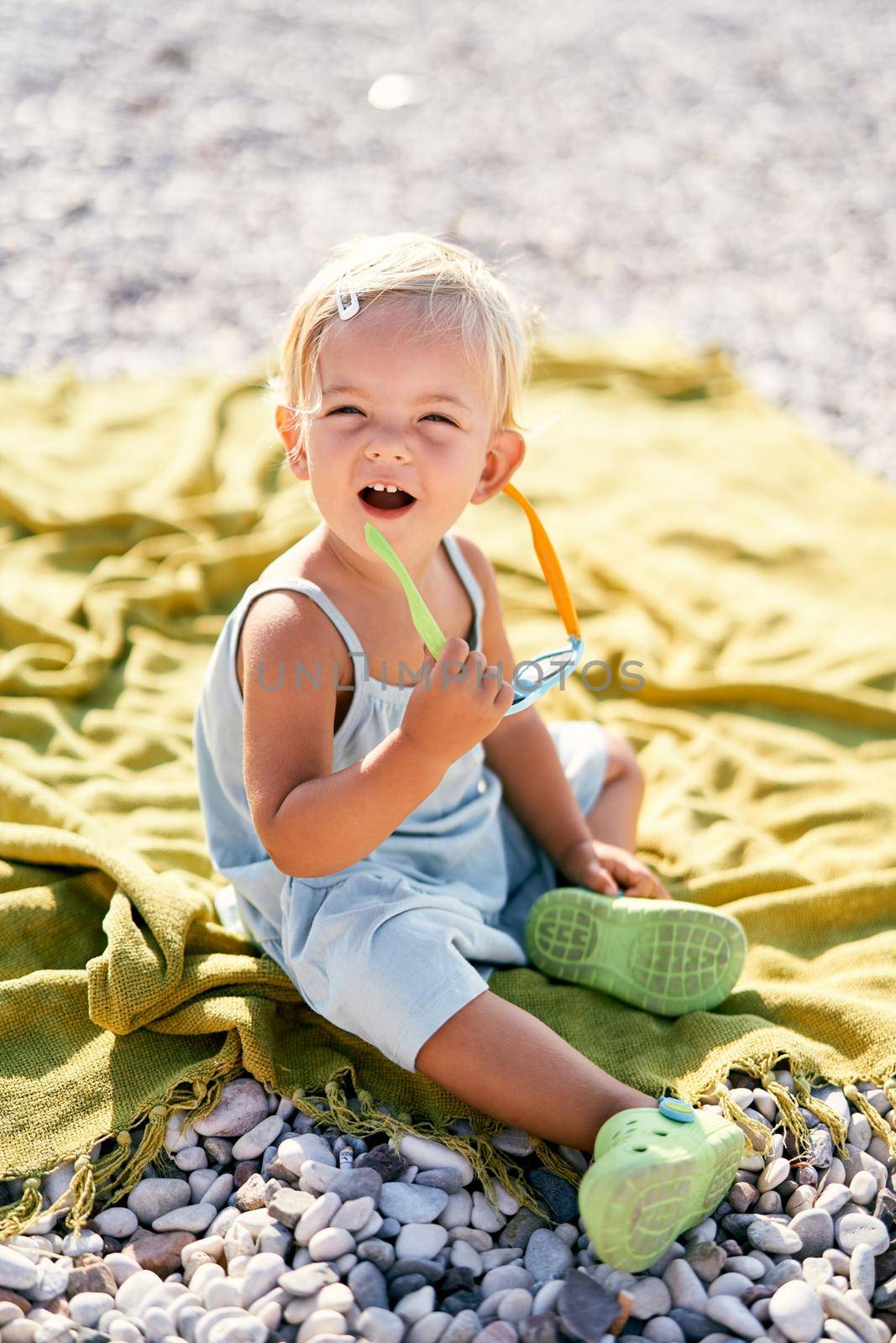Little girl laughing while taking off her sunglasses on a blanket on the beach. High quality photo