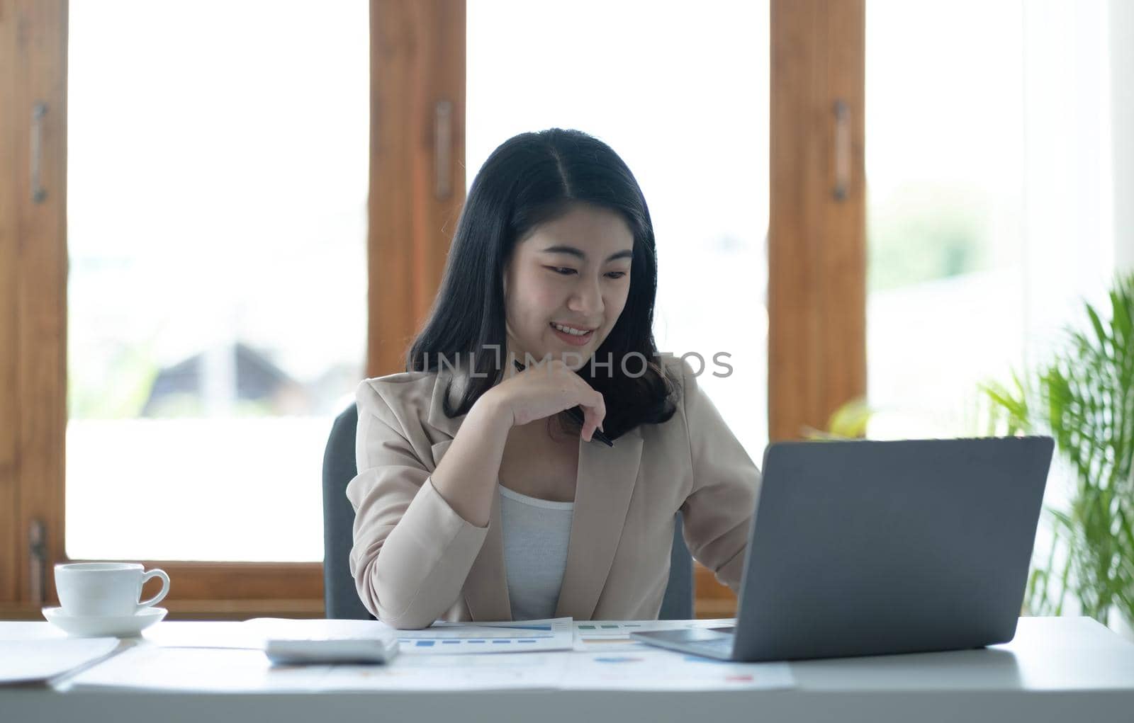 Beautiful young asian woman sitting at coffee shop using laptop. Happy young businesswoman sitting at table in cafe with tab top computer. by wichayada