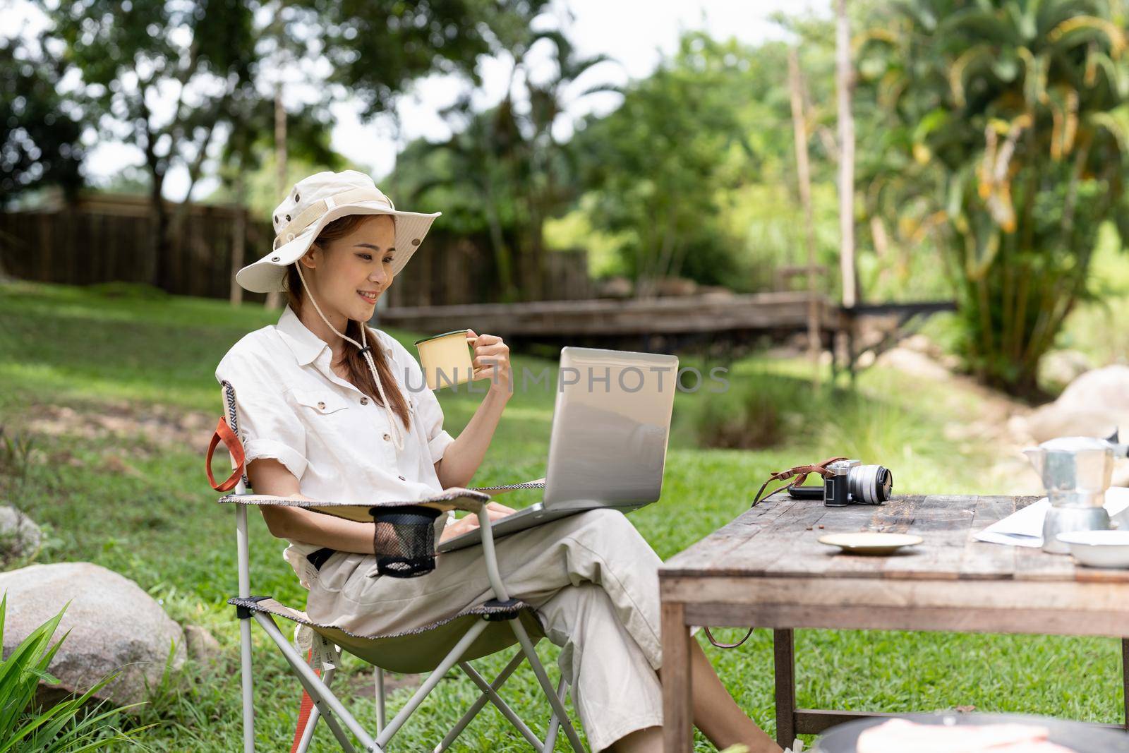 Young girl using laptop in camping tent, hiking in forest.