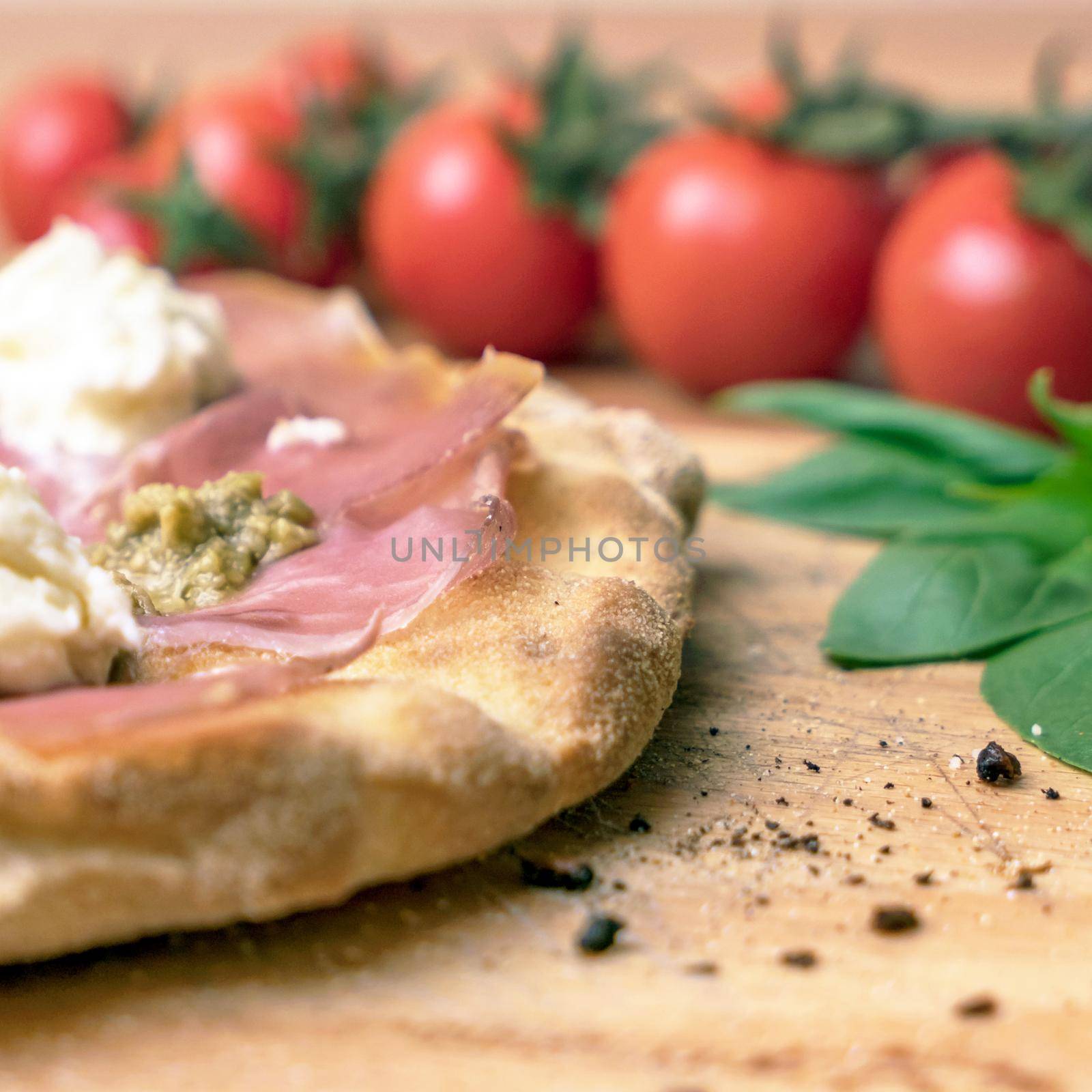 Italian pizza close-up. Close up of italian pizza on a wooden cutting board. On background defocused tomatoes and basil.