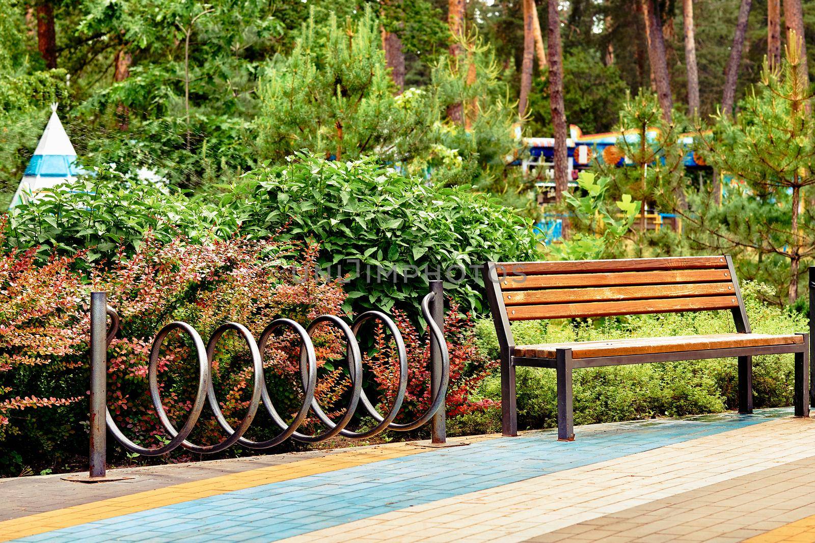 Wooden bench and bike rack in a green city park with rides and trees by jovani68