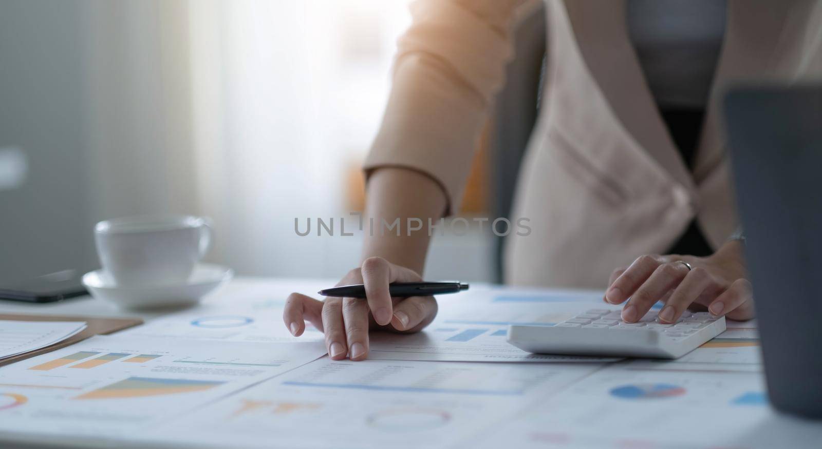 Close up a Business woman using calculator and laptop for doing math finance on a wooden desk, tax, accounting, statistics, and analytical research concept by wichayada