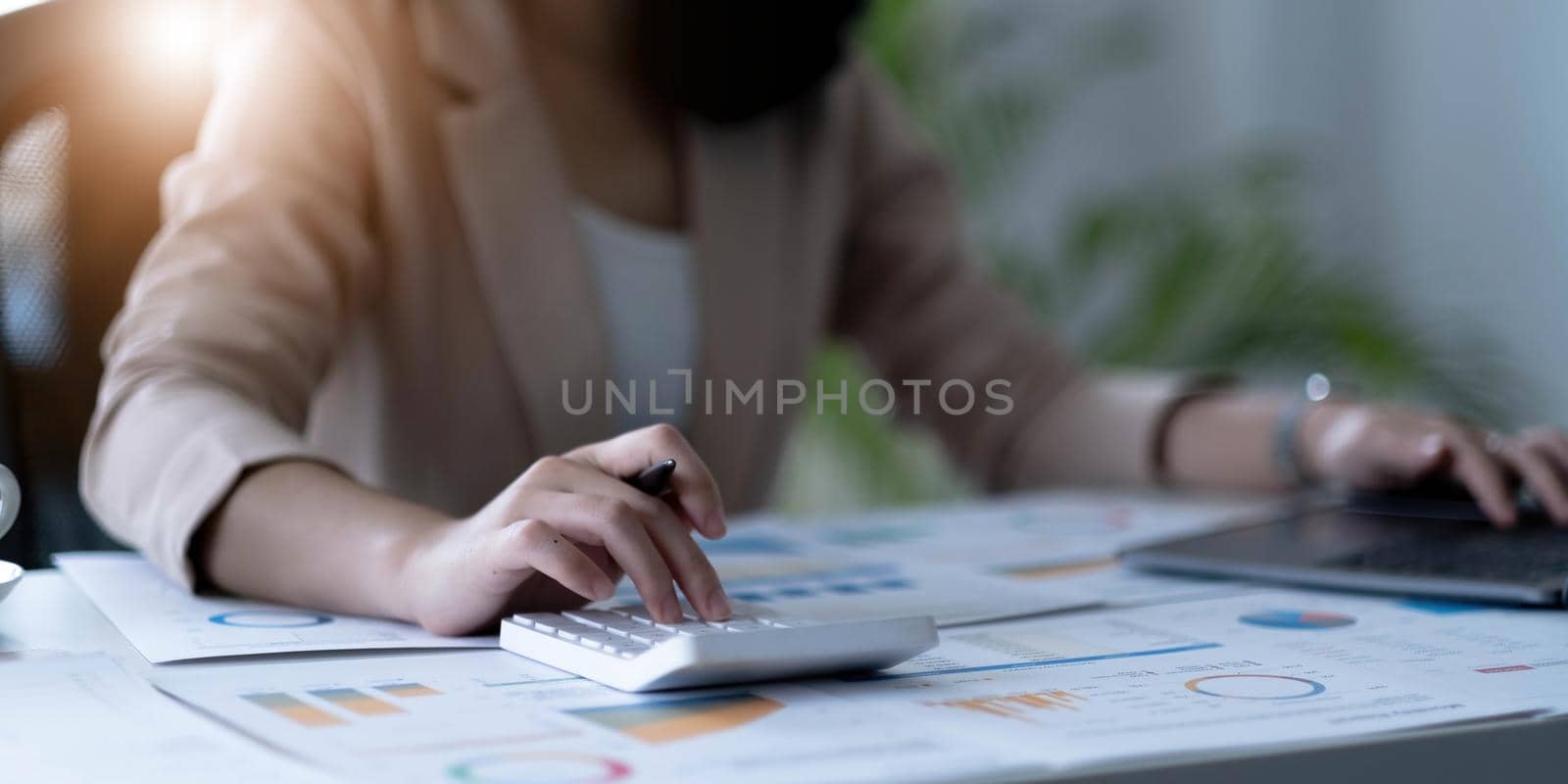 Close up Business woman using calculator and laptop for do math finance on wooden desk in office and business working background, tax, accounting, statistics and analytic research concept.