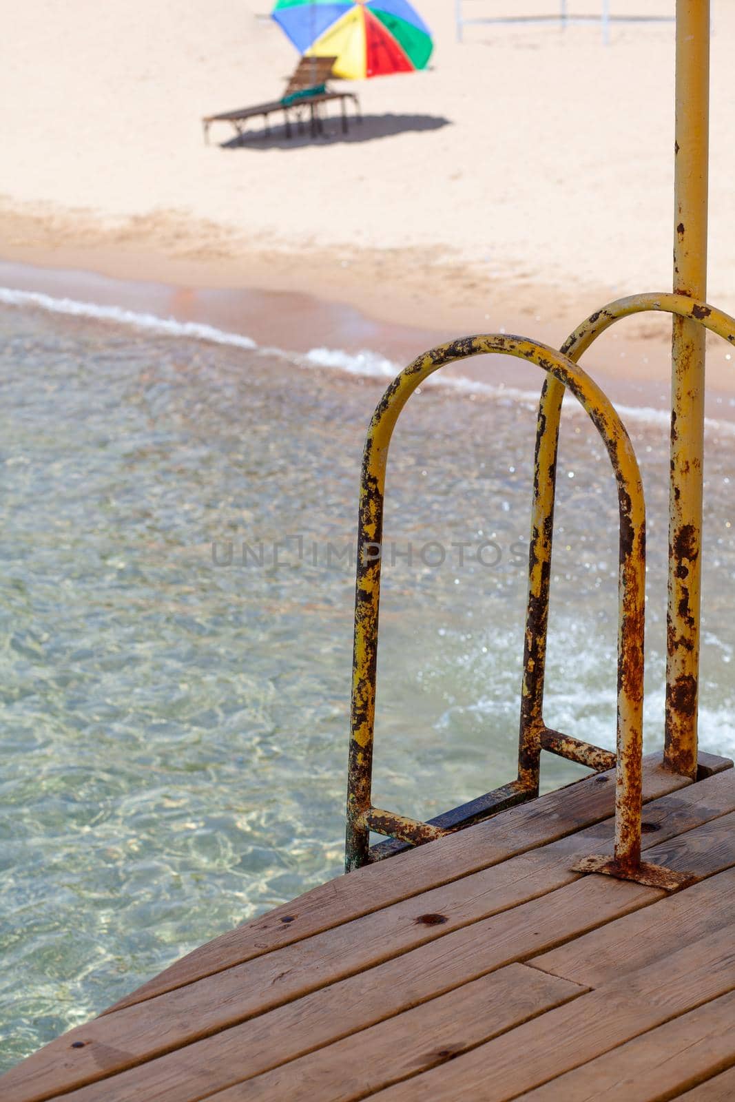 Swimming area or pier on the sea. A large pier with a roof, wooden planks and rusty stairs descending into the water. Bathing and resting place.