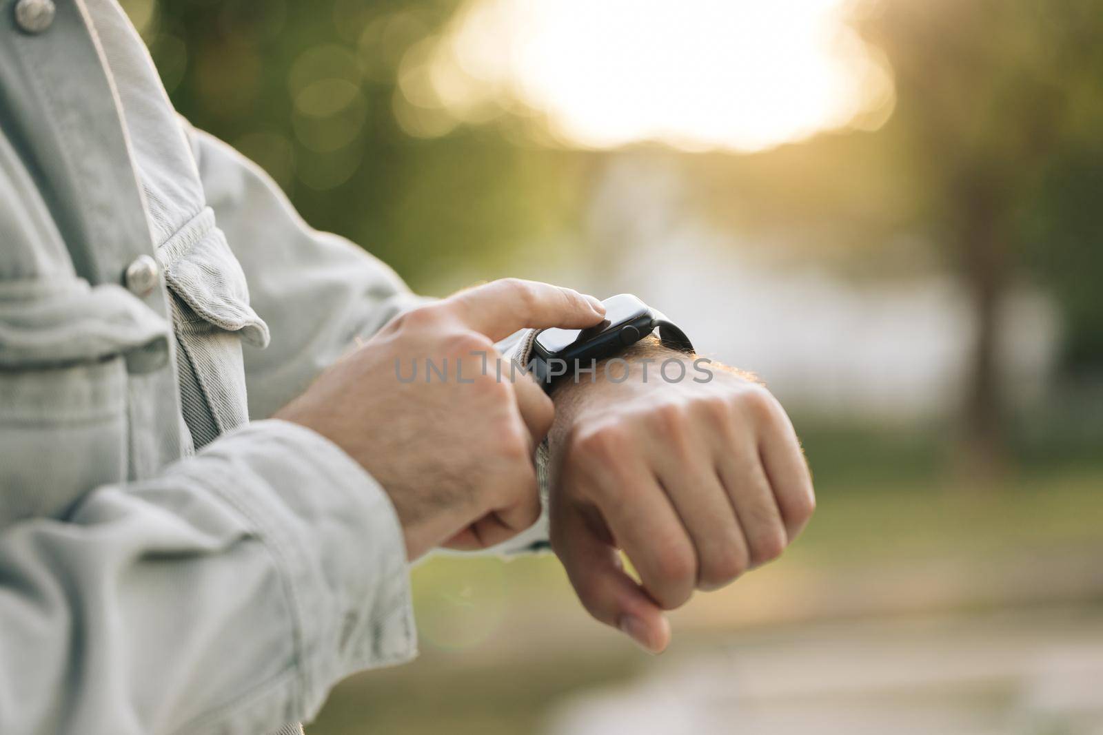 Smart watch on a man's hand outdoor. Man's hand touching a smartwatch. Close up shot of male's hand uses of wearable smart watch at outdoor in sunset. Smart watch.