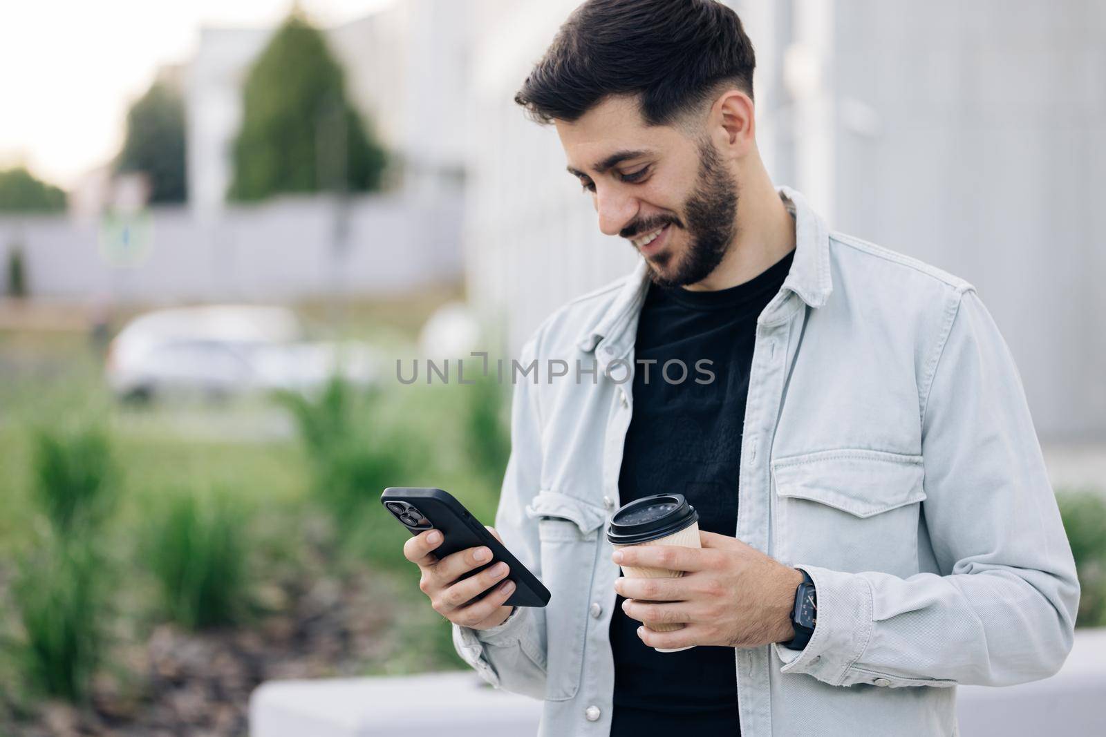 Smiling young attractive bearded man walking use smartphone look around at city center. Handsome man messagen stylish. Employment technology.