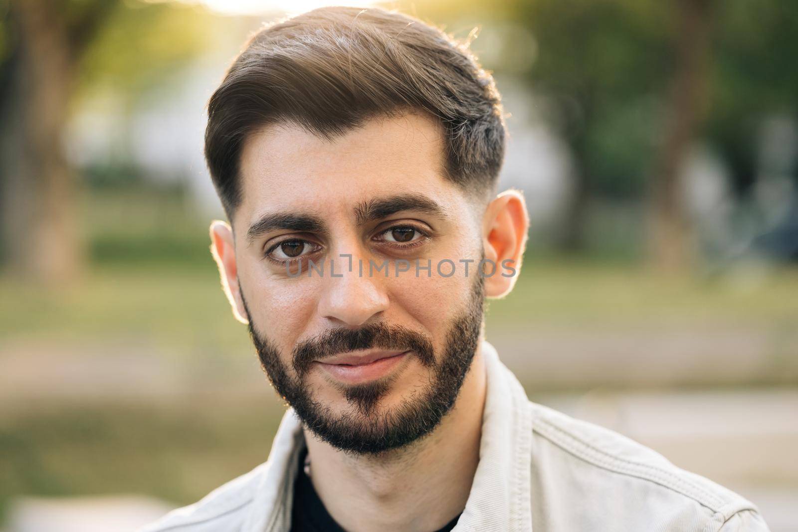 Face of caucasian ukrainian man looking at camera. Portrait young pretty brunette guy outside at sunshine. Etnnicity. People. Beauty.