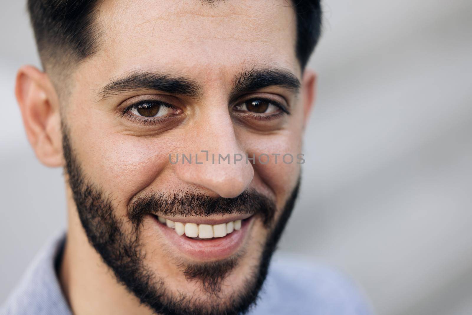 Portrait of attractive joyful young caucasian mixed race man in business formal suit smiling and posing near modern buildings outside. Businessman. Ethnicity.